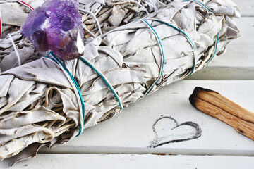 A close up image of healing white sage smudge bundles white healing crystals on a white table top. 