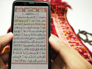 Man reading holy Quran on his smartphone after praying