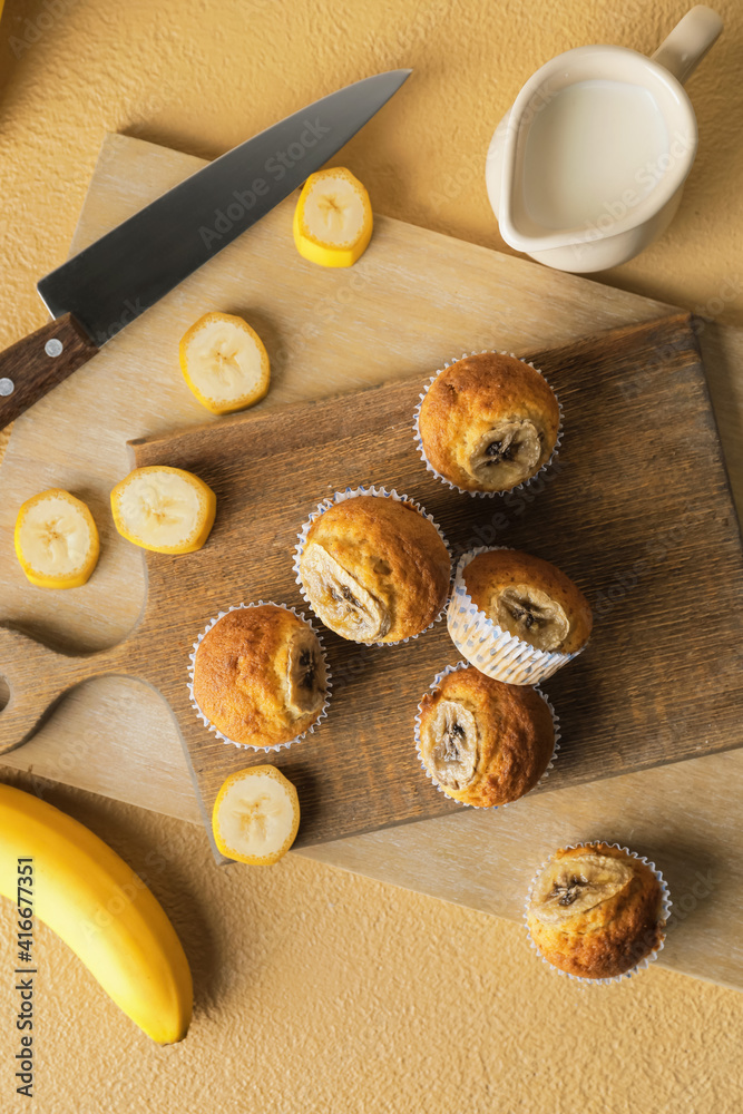 Board with tasty banana muffins on color background