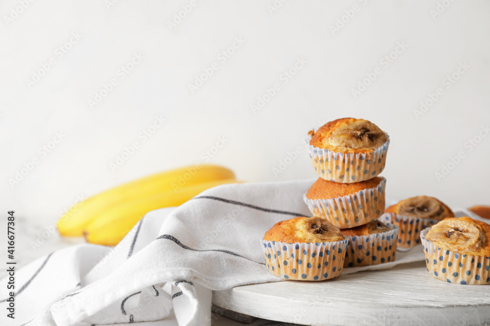 Board with tasty banana muffins on light wooden background