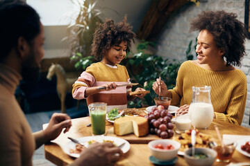 Happy African American girl having breakfast with her parents at dining table.