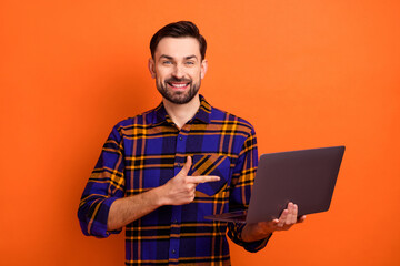 Photo of positive man indicate finger hand hold laptop beaming smile isolated on orange color background