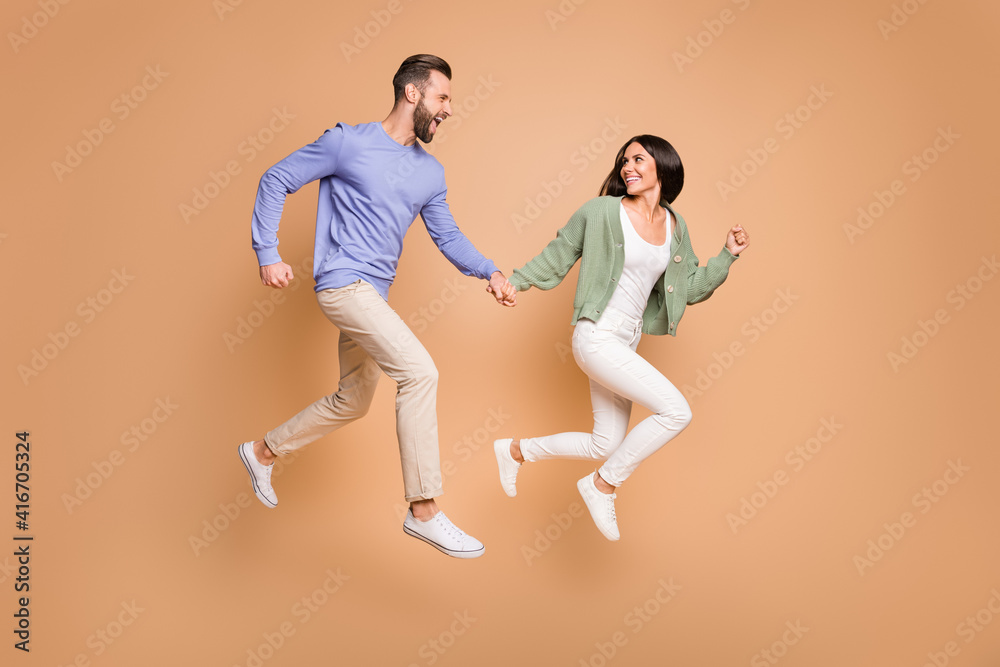 Full length body size view of nice cheerful life partners jumping holding hands running leisure isolated on beige pastel color background - obrazy, fototapety, plakaty 