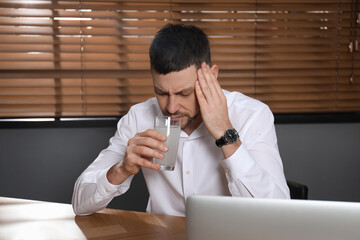 Wall Mural - Man taking medicine for hangover at desk in office