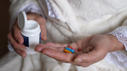 Senior adult woman taking medicine in pills. Pours out of bottle on palm hand capsules of vitamin analgesic antibiotics antiviral. Old people senior takes medicine and health care. Close up view