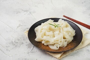 Wall Mural - Grainy look Fresh Kwetiau as White Chinese noodles made from Rice in black plate. Popular in South East Asia on texture white background