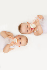 two baby twins boy and girl with a bottle of milk on a white bed at home, baby food concept, place f