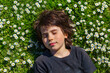 © Anna - Close up portrait of a young boy lying on a glade with daisies and closing eyes with pleasure. Child wearing dark grey t shirt resting on a grass in the park in summer or spring.