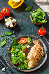 Healthy food. Ketogenic diet lunch. Grilled chicken fillet with fresh vegetable salad, spinach and feta on a dark stone background.