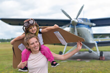 A Caucasian Woman And Her Little Daughter Are Playing A Pilot Against The Backdrop Of A Small Plane With A Propeller