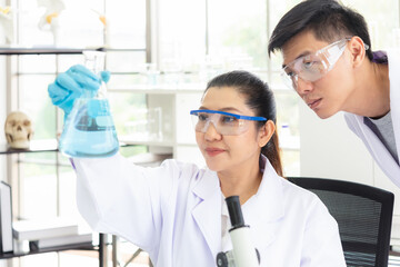 Wall Mural - team work asian woman and man scientists analyzing study data and evaluating microscope success for 