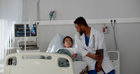 Young african doctor sitting on hospital bed and talking to preteen boy patient