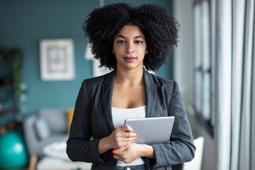 Wall Mural - Smart afro young entrepreneur woman using her digital tablet while standing looking at camera in the office at home.