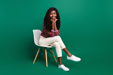 Wall Mural - Photo of sweet dreamy curly dark skin woman dressed red shirt sitting chair arms chin isolated green color background