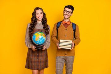 Poster - Photo of brunette happy school guy and girl hold globe textbooks smile wear glasses isolated on yellow color background