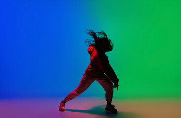 Wall Mural - Night. Stylish sportive girl dancing hip-hop in stylish clothes on colorful background at dance hall in neon light. Youth culture, movement, style and fashion, action. Fashionable bright portrait.