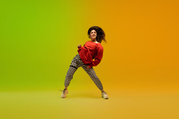 Wall Mural - Action. Stylish sportive girl dancing hip-hop in stylish clothes on colorful background at dance hall in neon light. Youth culture, movement, style and fashion, action. Fashionable bright portrait.
