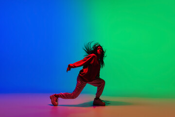Wall Mural - Moving. Stylish sportive girl dancing hip-hop in stylish clothes on colorful background at dance hall in neon light. Youth culture, movement, style and fashion, action. Fashionable bright portrait.