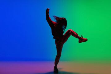 Wall Mural - Modern. Stylish sportive girl dancing hip-hop in stylish clothes on colorful background at dance hall in neon light. Youth culture, movement, style and fashion, action. Fashionable bright portrait.