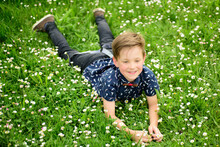 Happy Child Boy Lying On Grass Background. Cute Kid Enjoying Carefree Lifestyle On Field Flower Lawn.
