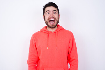 Sticker - Surprised young Caucasian bearded man wearing pink hoodie against white background, shrugs shoulders, looking sideways, being happy and excited. Sudden reactions concept.