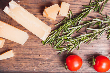 Pieces of hard, aged cheese parmesan, fresh tomatoes and herbs on wooden board