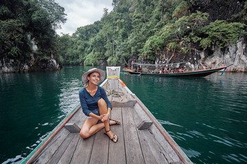 Wall Mural - Happy vacation in Thailand. Pretty young woman taking sailing Khao Sok National Park lake on traditional longtail boat.