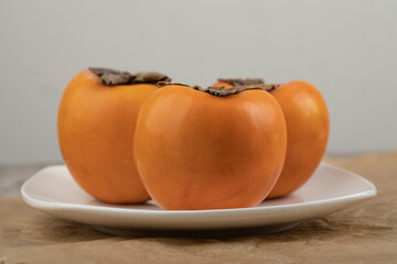 Three tasty fuyu persimmon on white plate on marble surface