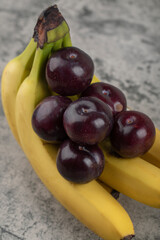 Wall Mural - Fresh healthy plums with banana cluster on stone background