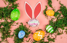 Bright Colorful Easter Eggs, Paper Rabbit Ears And Green Moss On A Pink Background. Top View