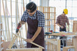 © Bangkok Click Studio - asian adult worker wearing safety glasses and plaid shirt stand drilling wooden stick with electric screwdriver when his colleague wearing yellow safety helmet working at table in blurred background