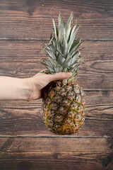 Female hand holding single fresh pineapple on wooden background