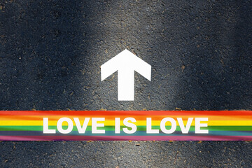 Love is love written on rainbow line marking with white arrow sign with on asphalt road. Lesbian gay bisexual transgender concept and equality diversity idea
