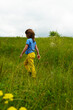 © LKoroleva - A six-year-old boy in yellow pants and a blue T-shirt with long hair walks in the meadow. Green grass and sky.