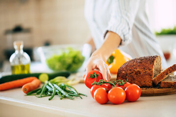 Wall Mural - Close up photo of young smiling woman is preparing a fresh healthy vegan salad with many vegetables in the kitchen at home and trying a new recipe