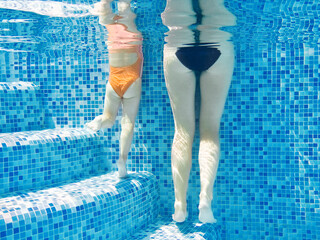 Wall Mural - Mother and kid in swimming pool, underwater legs of woman and child in pool water, family vacation
