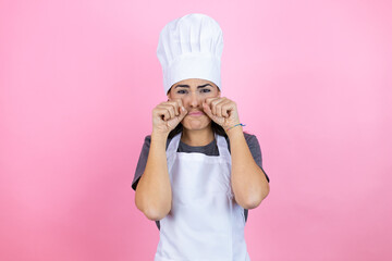 Wall Mural - Young hispanic woman wearing baker uniform over pink background depressed and worry for distress, crying angry and afraid. Sad expression.