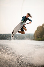 Young Adult Guy Jumps Spectacularly On Wakeboard Above The Water With Splashes