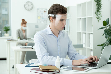 Poster - Young serious businessman in protective screen on head looking at laptop display