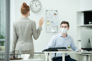 Poster - Back of young businesswoman waving hand to her male colleague in protective mask