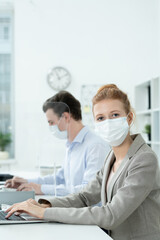 Poster - Young female office manager in protective mask and elegant suit using laptop