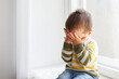© Evrymmnt - Portrait of adorable little boy sitting on the windowsill and crying. Upset child covering his face at home. Barefoot kid hiding behind palms of his hands. Close up, copy space, background.