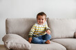 © Evrymmnt - Portrait of adorable little boy sitting on the textile couch and smiling. Happy toddler laughing and being playful at home. Barefoot kid in denim pants. Close up, copy space, background.