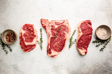 Wall Mural - Variety of Fresh Raw Black Angus Prime Meat Steaks T-bone, New York, Ribeye and seasoning on white background, top view