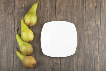 White plate and delicious ripe pears on wooden surface