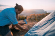 © Anna - Young male tourist puts a tent in the mountains.