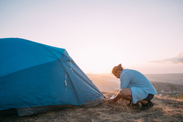 young male tourist puts a tent in the mountains.