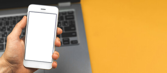 Smartphone mockup, yellowand bright desktop or workspace conceptwith laptop, phone in a hand with blank white screen