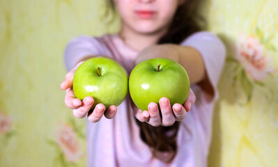 The girl holds two green apples in her hands. Blurry.