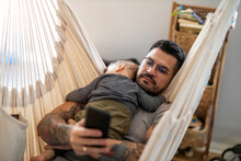 Man Checking His Phone While His Little Baby Son Is Sleeping
